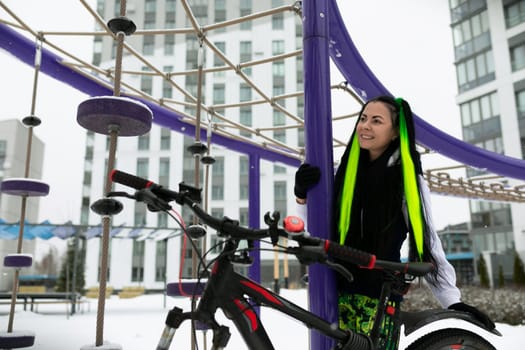 A woman is standing next to a bike in a snowy outdoor setting. She is dressed warmly as she examines the bicycle, which is covered in snow.