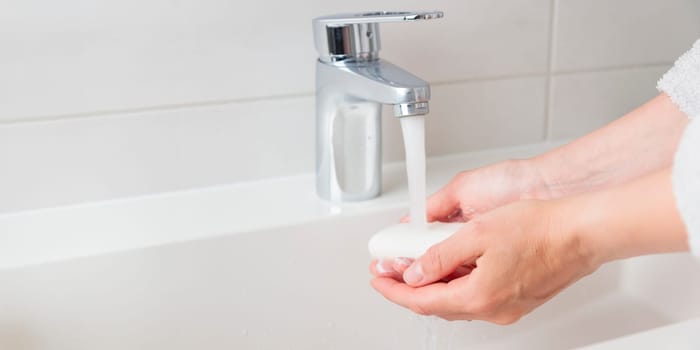 Banner of woman's soapy hands with running water in sink, cleaning skin care concept, white minimalistic bathroom