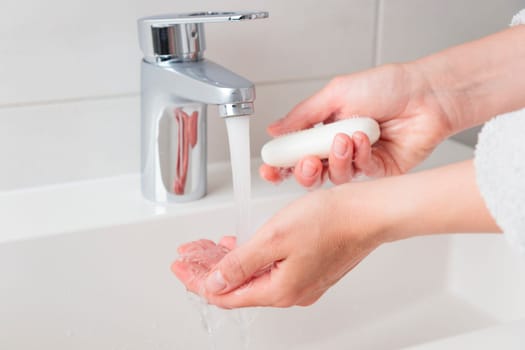 Woman washing cleansing soapy hands in bathroom to prevent virus infection, cleaning skin care in foam, chrome faucet and white sink and a piece of soap