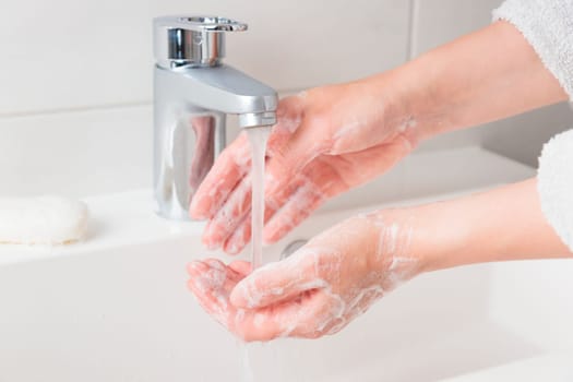 Woman washing cleansing soapy hands in bathroom to prevent virus infection, cleaning skin care in foam, rubbing hands rinsing with running water. Bacteria protection concept. Close up view