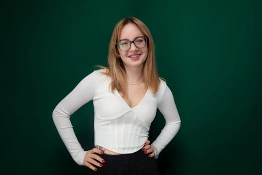 A woman wearing glasses is striking a pose for a photograph. She stands confidently, smiling at the camera with her hands on her hips. The background is simple, allowing the focus to be on her. The image captures a moment of self-assuredness and style.