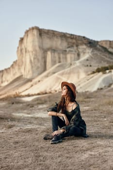 Woman wearing hat sits in front of mountain, admiring scenic view on sunny day