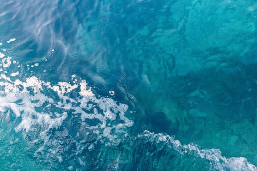 Beautiful view of blue colored water with white foamy wave on the left on a sunny summer day, close up view from above.