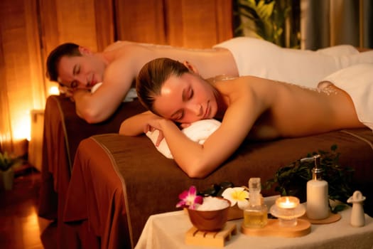 Couple customer having exfoliation treatment in luxury spa salon with warmth candle light ambient. Salt scrub beauty treatment in Health spa body scrub. Quiescent