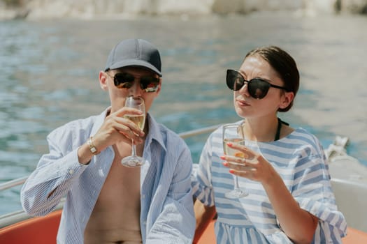 Portrait of one young Caucasian beautiful brunette couple in sunglasses drinking champagne from glasses while sitting in a boat while sailing on the sea on a sunny summer day, close-up side view.