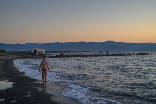 A girl is walking along island coastline at the sunset time.