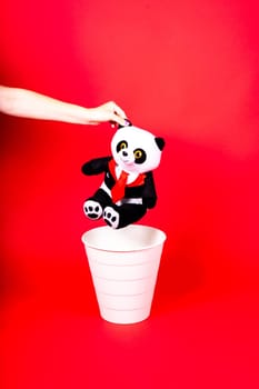 Woman putting the broken toys in waste bin on red background, copy space