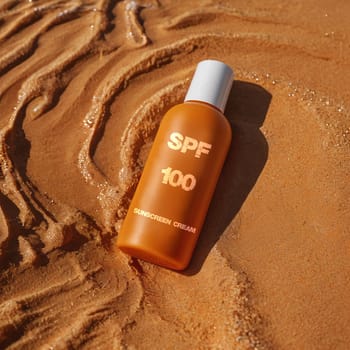 SPF 100 sunscreen in orange bottle. High quality photo. Sunscreen. Summer cream. Tanning product. Tanning remedy. Cream on vacation and vacation. Cream on the seashore on wet sand