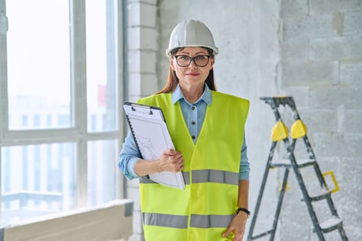 Portrait of woman builder engineer architect supervisor at construction. Confident middle-aged female in vest helmet looking at camera. Construction industry technical professions work engineering