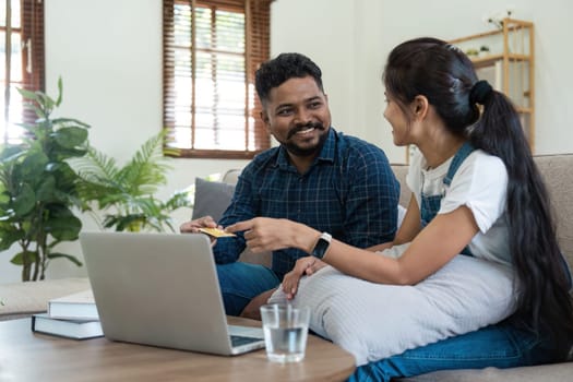 An Indian couple sitting in their living room, using a laptop to pay bills and plan their finances together. They are engaged in a discussion, showcasing teamwork and modern financial management.