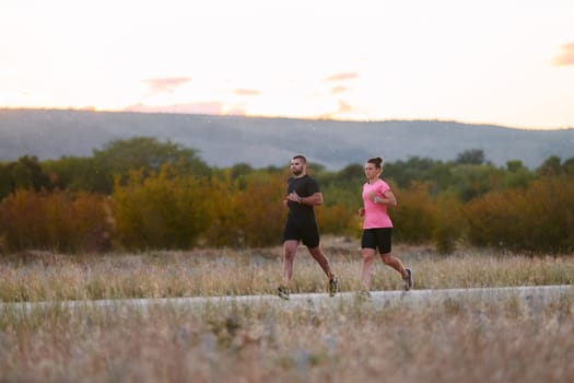 A couple dressed in sportswear runs along a scenic road during an early morning workout, enjoying the fresh air and maintaining a healthy lifestyle