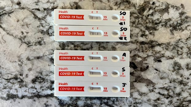 Denver, Colorado, USA-August 28, 2023-A close-up image of five iHealth COVID-19 test kits placed on a marble countertop. Each test shows negative results, with some kits marked with letters and numbers.