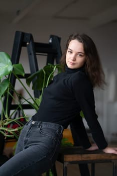 young beautiful woman posing in a black sweater near the window