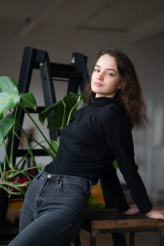 young beautiful woman posing in a black sweater near the window