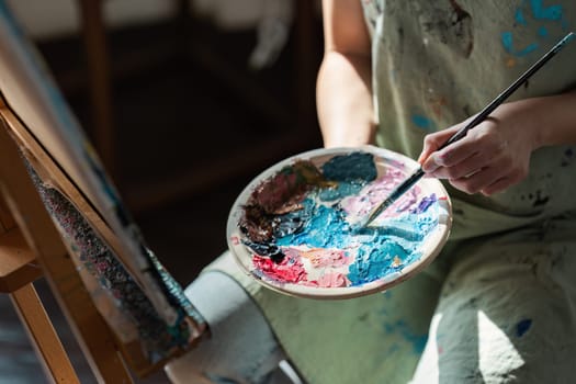 A person engaged in the hobby of painting, holding a palette with various colors, and working on a canvas in a well-lit studio.