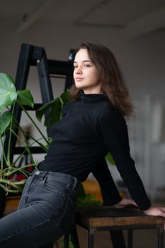 young beautiful woman posing in a black sweater near the window