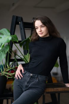 young beautiful woman posing in a black sweater near the window