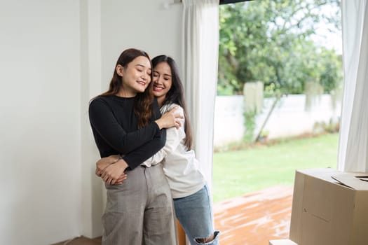 Lesbian couple embracing in their new home, celebrating moving day. LGBT love and modern lifestyle concept with cardboard boxes in a bright, welcoming house.