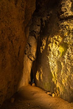 A narrow tunnel with a small opening in the middle. The tunnel is dark and the light is coming from the right