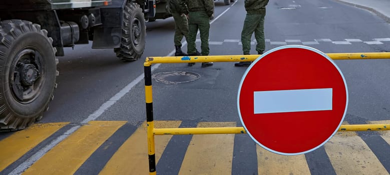 Armed soldiers at a roadblock with a no entry sign. Soldiers in full gear, carrying rifles. Roadblock made of metal barriers. No entry sign is large and red with a white border.