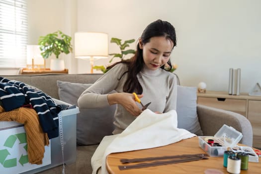 Woman cutting old clothes for recycling at home, promoting sustainable living and environmental conservation.