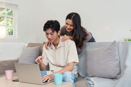 Happy couple sitting on a sofa, using a laptop, and enjoying their time together in a cozy and bright living room.