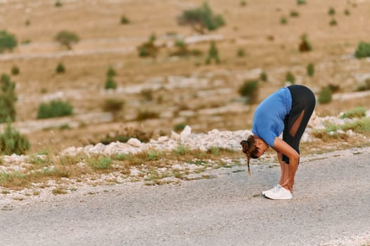 A determined female athlete stretches her muscles after a strenuous run through rugged mountain terrain, surrounded by breathtaking rocky landscapes.