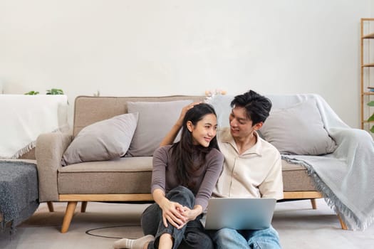 A couple sitting on the floor in front of a sofa, using a laptop, enjoying a relaxed moment at home. Modern interior with cozy and comfortable ambiance.