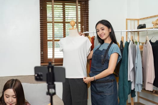 Young e-business owner livestreaming fashion products, showcasing clothing on a mannequin, and engaging with customers from a home office.