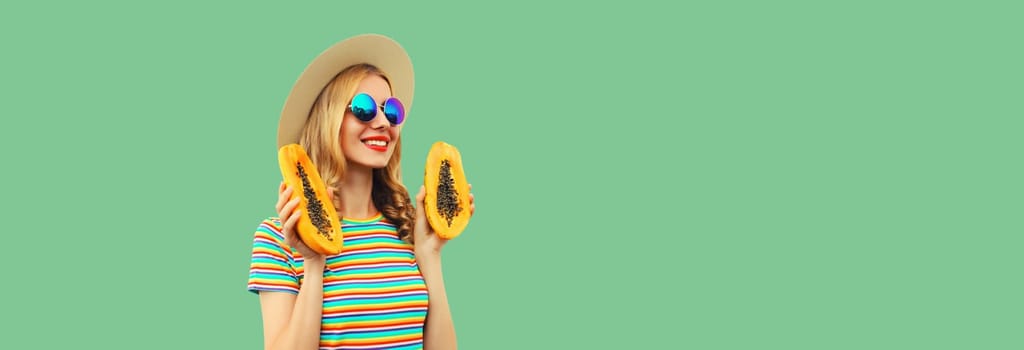 Summer portrait of happy cheerful young woman having fun with fresh papaya fruits wearing straw hat, sunglasses on green background, copy space