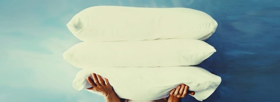 Healthy sleep, woman holds pile of folded white pillows in her hands at home