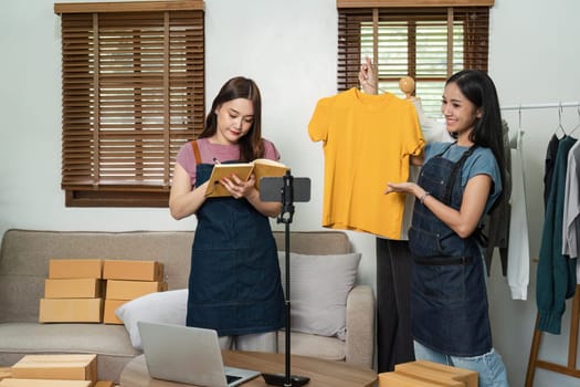 Two young women managing their online clothing business from home, organizing inventory, and creating content for their e-commerce store.