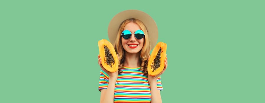 Summer portrait of happy cheerful young woman having fun with fresh papaya fruits wearing straw hat, sunglasses on green background, copy space