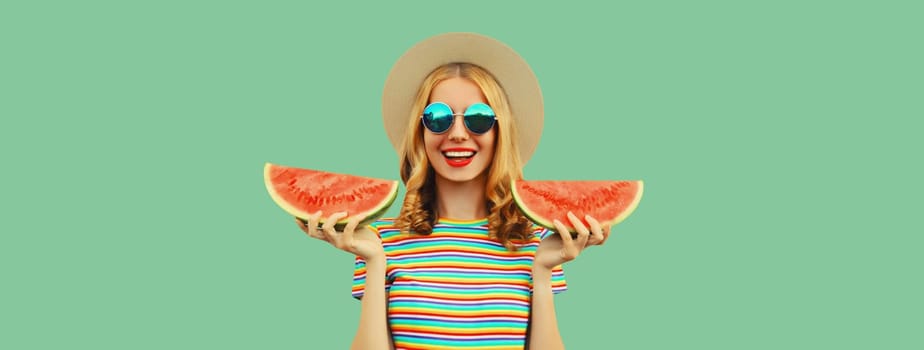 Summer portrait of happy young woman eating fresh slice of watermelon in straw tourist hat, sunglasses on green studio background