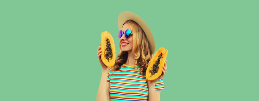 Summer portrait of happy cheerful young woman having fun with fresh papaya fruits wearing straw hat, sunglasses on green background, copy space