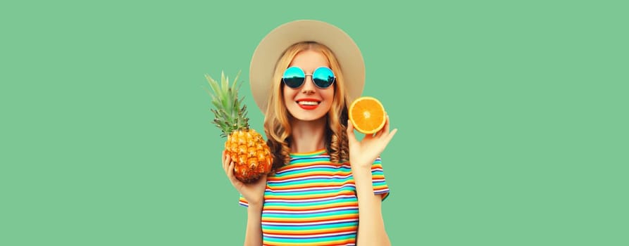 Summer portrait of happy smiling young woman with pineapple, orange fruit in straw tourist hat, sunglasses on green studio background