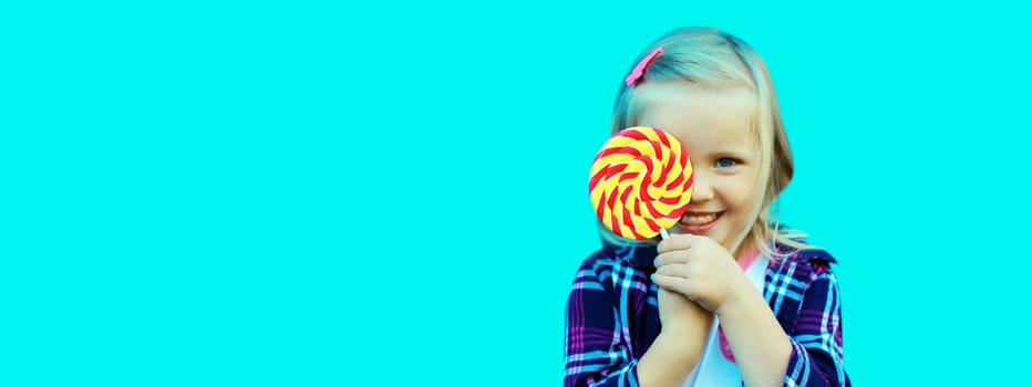 Portrait of happy cheerful smiling little girl child with sweet lollipop on stick on blue background, blank copy space for advertising text