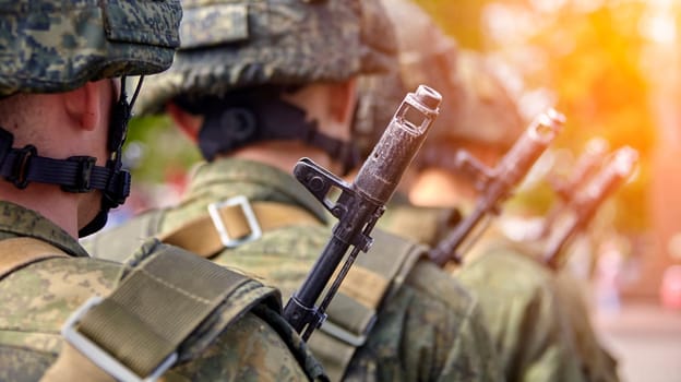 A soldier in full gear stands at attention with a rifle, wearing a helmet and camouflage uniform. Blurred background adds focus and determination to his readiness and vigilance.