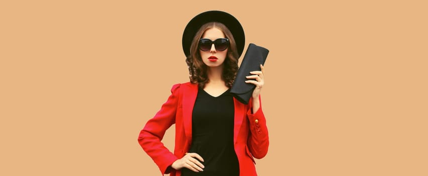Stylish elegant woman posing in business suit, red blazer jacket, black round hat with handbag clutch posing on brown studio background