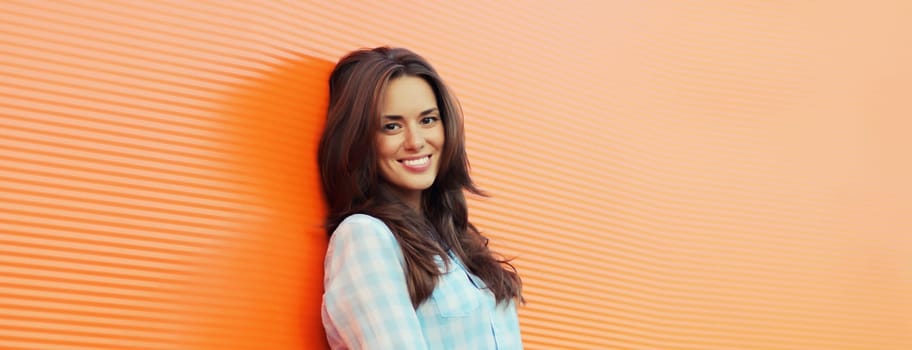 Portrait of beautiful happy smiling brunette young woman posing in the city on orange background