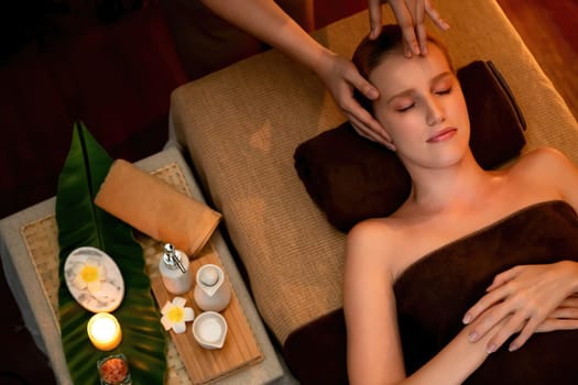 Caucasian woman enjoying relaxing anti-stress head massage and pampering facial beauty skin recreation leisure in warm candle lighting ambient salon spa in luxury resort or hotel. Quiescent