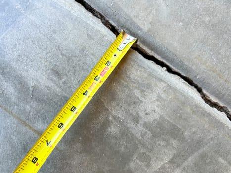 Close-up of a measuring tape placed along a concrete joint in a driveway. The image captures the process of assessing the width of the joint for repair work, highlighting the attention to detail in home maintenance.