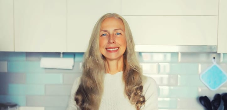 Portrait of happy smiling confident middle aged woman housewife with gray hair in the kitchen at home looking at camera