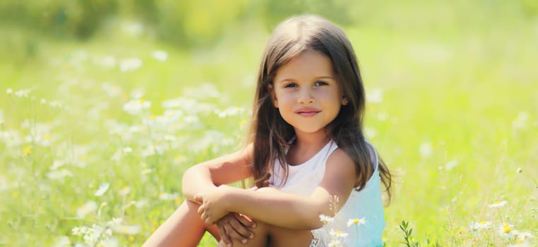 Portrait of happy little girl child sitting on grass in sunny summer park