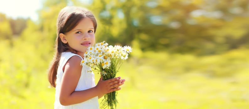 Portrait of cute little girl child with wildflowers in sunny summer park