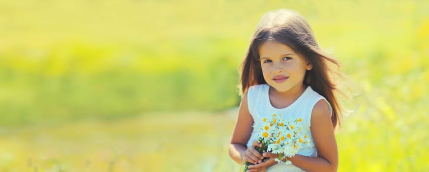 Portrait of cute little girl child with wildflowers in sunny summer park
