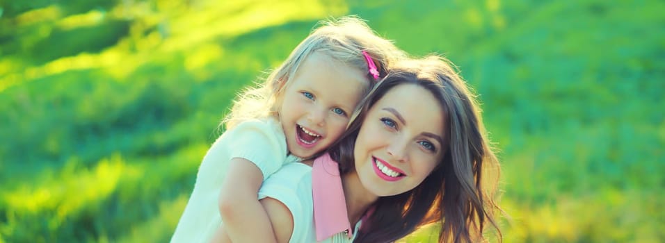 Portrait of happy cheerful smiling mother with little girl child daughter on the grass in sunny summer park