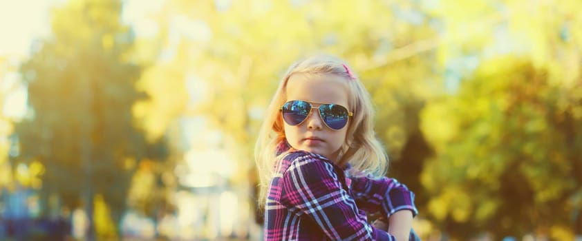 Stylish little kid girl posing in sunglasses looking away in sunny summer park