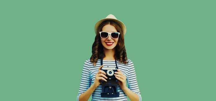 Summer portrait of happy smiling young woman photographer with film camera wearing summer straw hat on green background