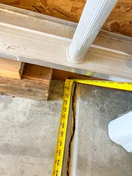 A close-up of a measuring tape placed along a foundation crack in a garage. The image captures the preparation for repair work, highlighting the importance of accurate measurements in foundation maintenance.
